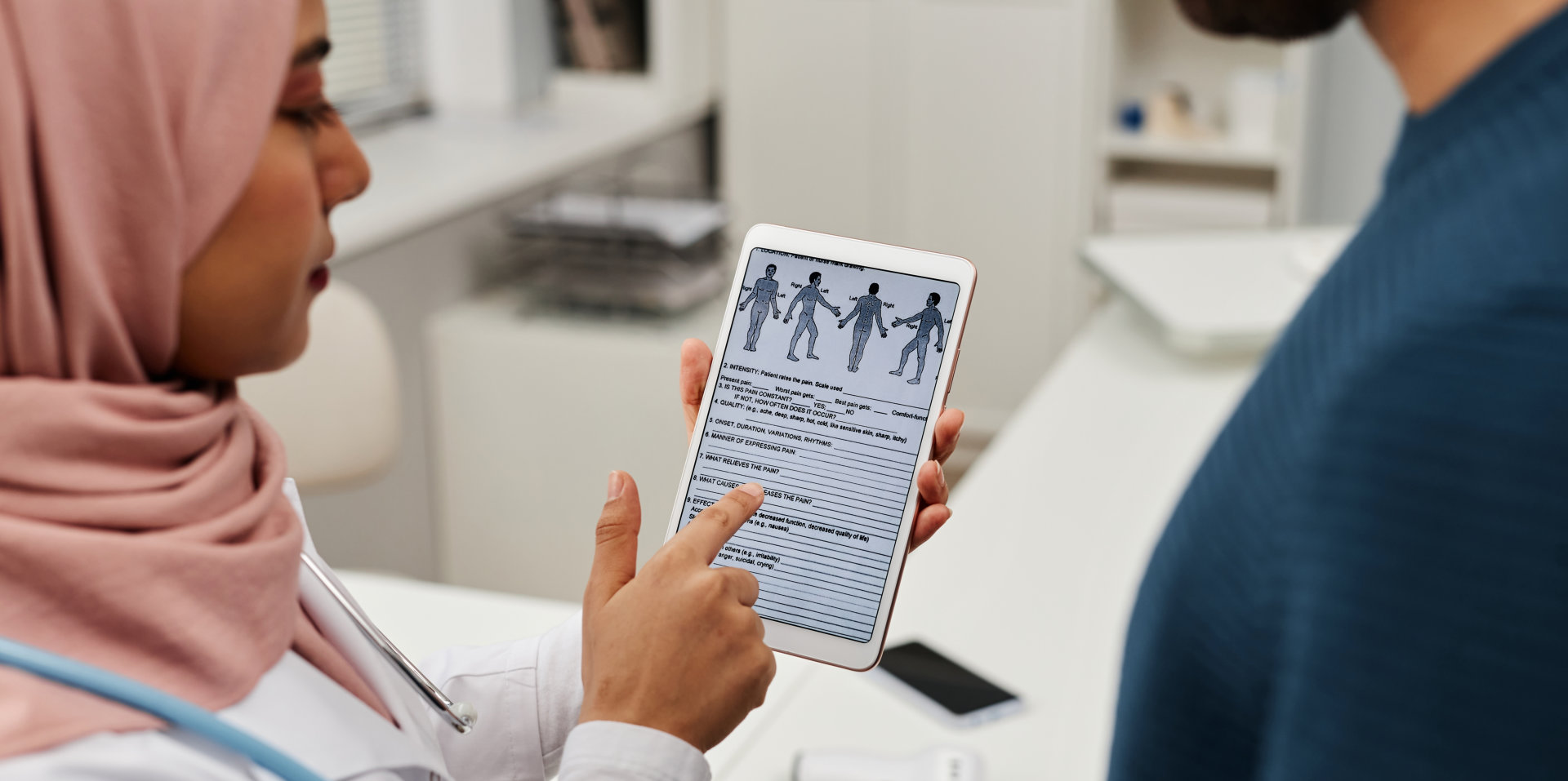 Muslim woman general practitioner in headscarf showing medical questionnaire on tablet screen to adult male patient