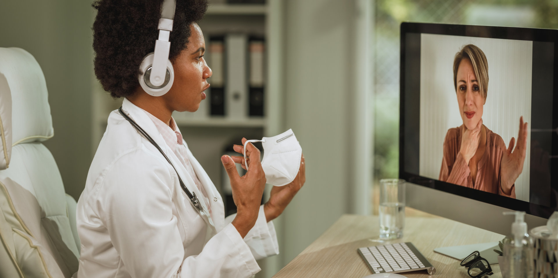 Shot of an African female doctor having video call with patient on computer in her consulting room during COVID-19 pandemic