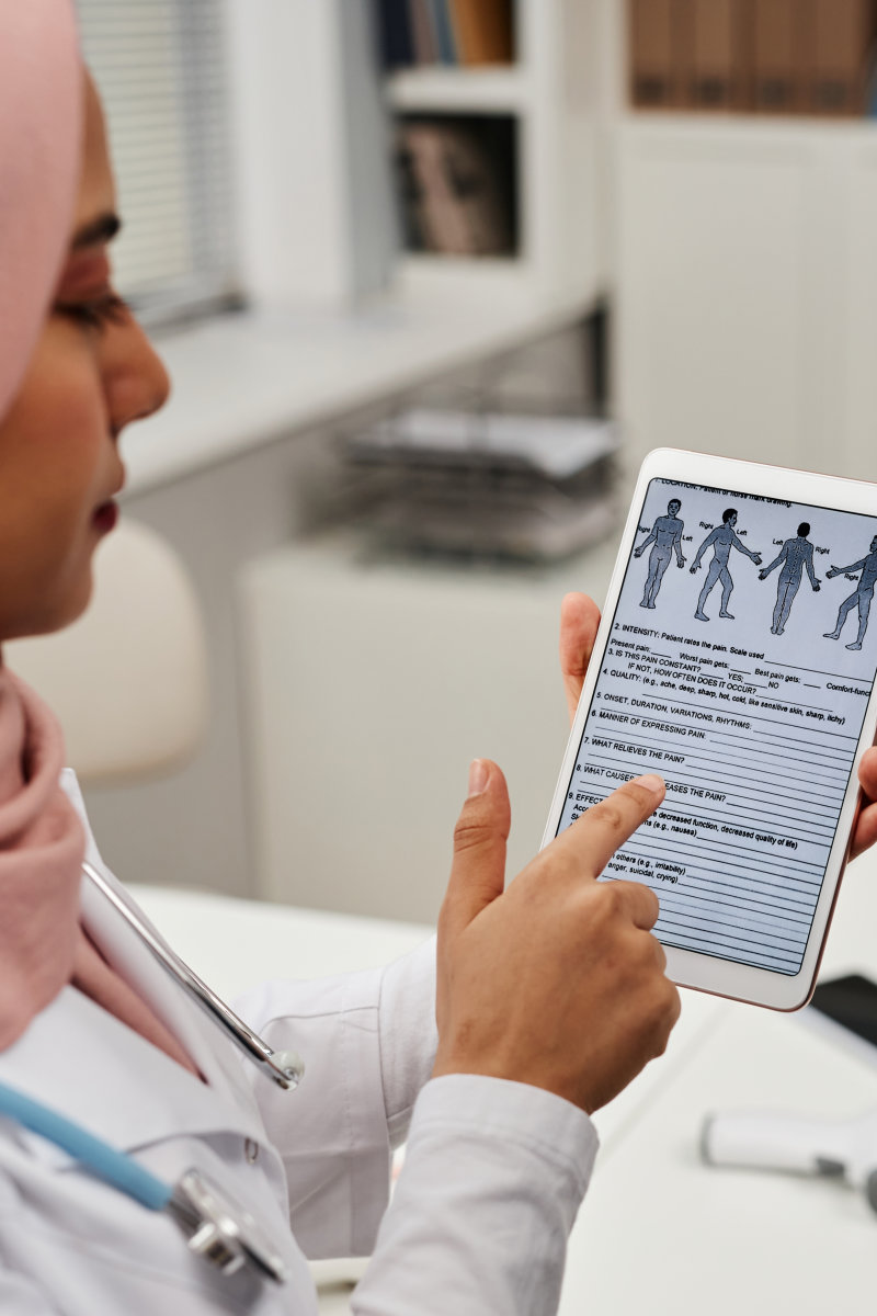 Muslim woman general practitioner in headscarf showing medical questionnaire on tablet screen to adult male patient