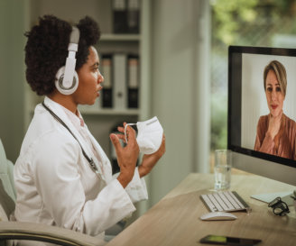 Shot of an African female doctor having video call with patient on computer in her consulting room during COVID-19 pandemic